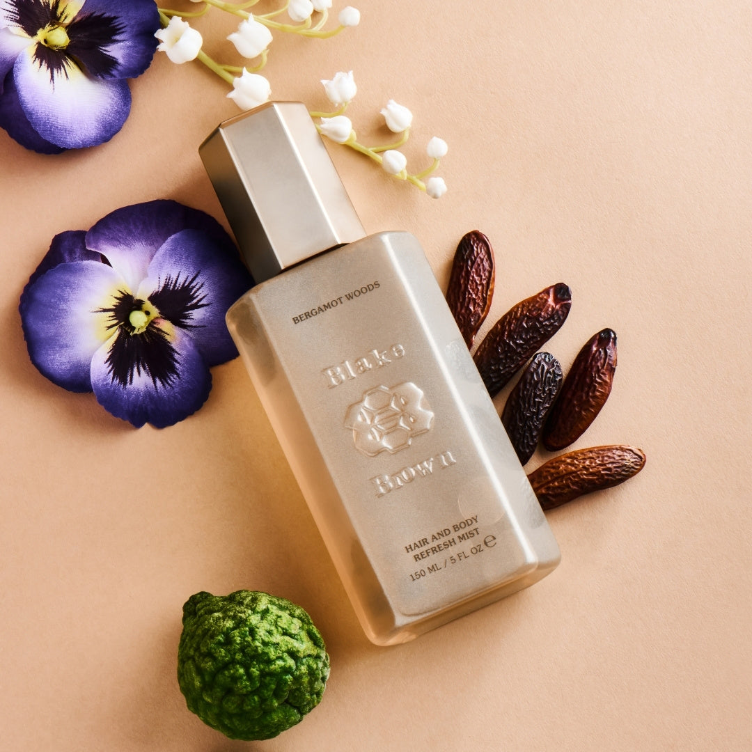 Blake Brown Hair and Body Refresh Mist in Bergamot Woods, styled with violets, lily of the valley, tonka beans, and a fresh bergamot fruit on a warm neutral background.