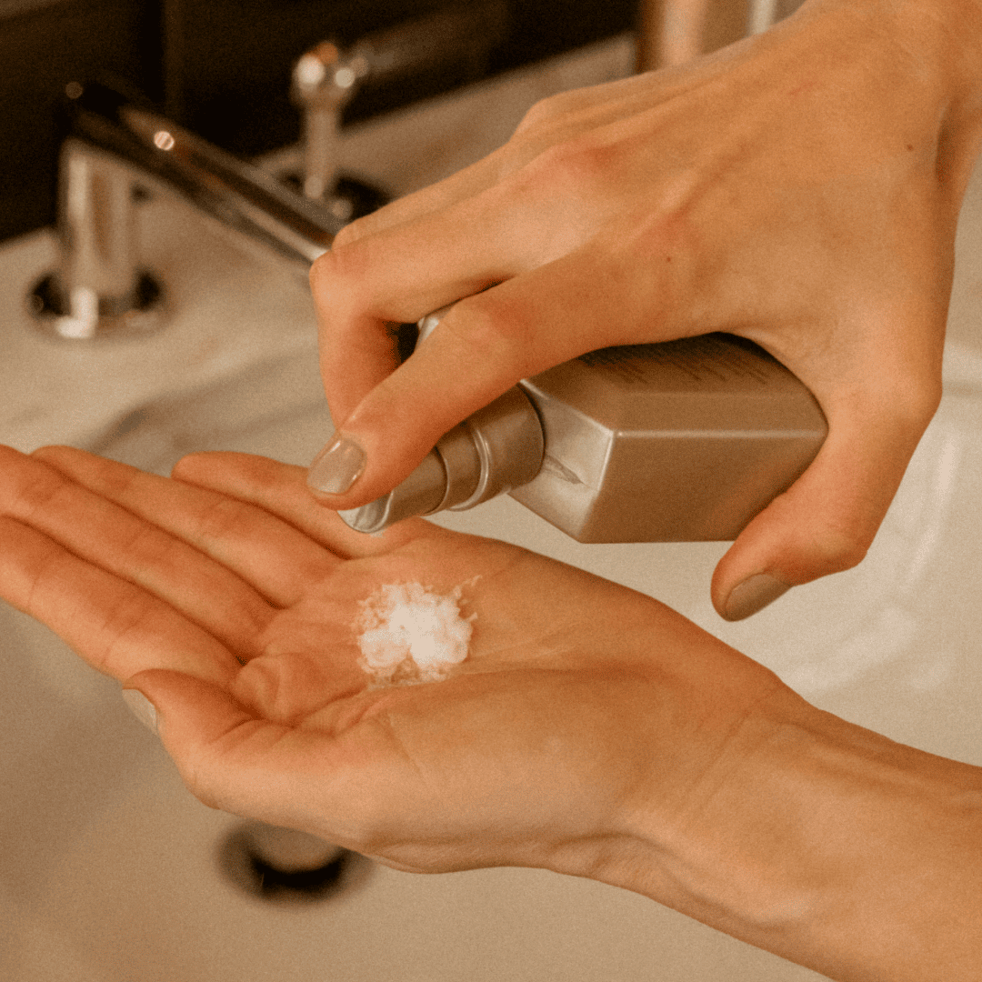 Hand dispensing Blake Brown Leave-In Potion into palm at the sink, showing its creamy texture.