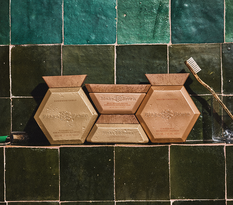 Blake Brown shampoo and mask duos in Sandalwood Vanille and Wild Nectar Santal displayed on a green tiled shelf with a toothbrush and glass jar.