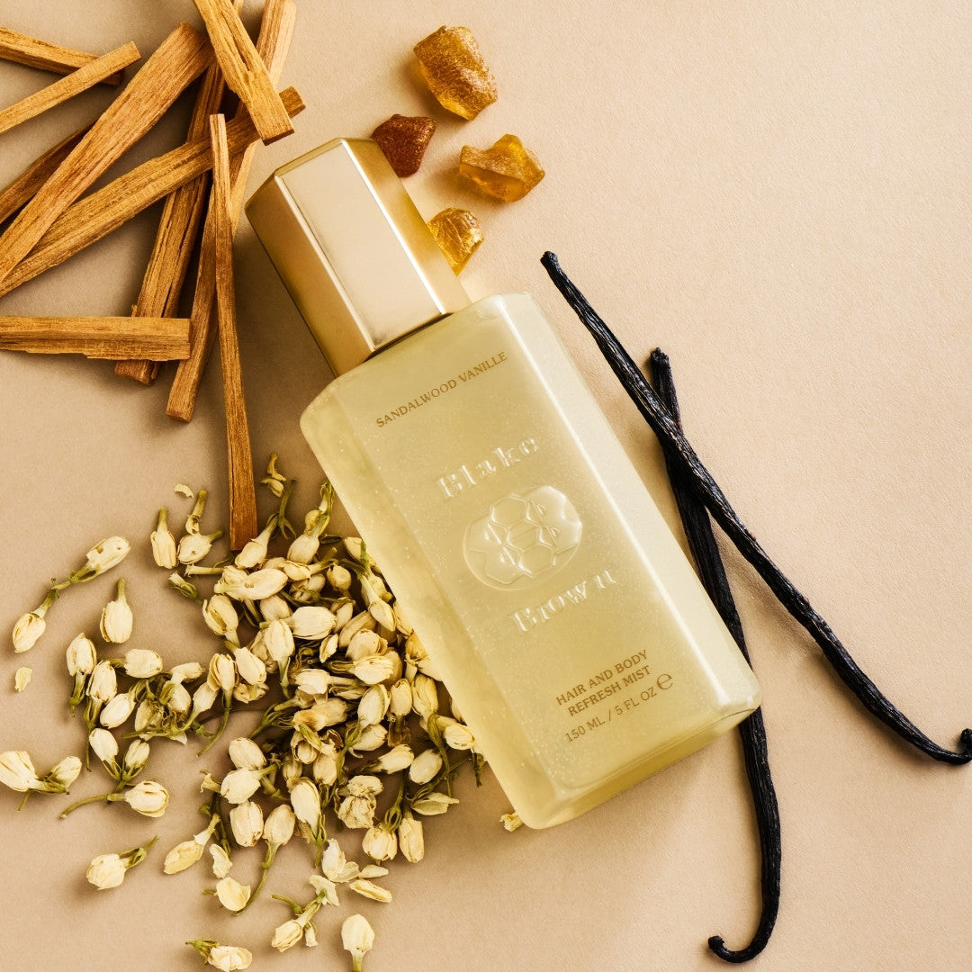 Blake Brown Hair and Body Refresh Mist in Sandalwood Vanille, surrounded by sandalwood sticks, vanilla beans, and jasmine blossoms on a neutral background.