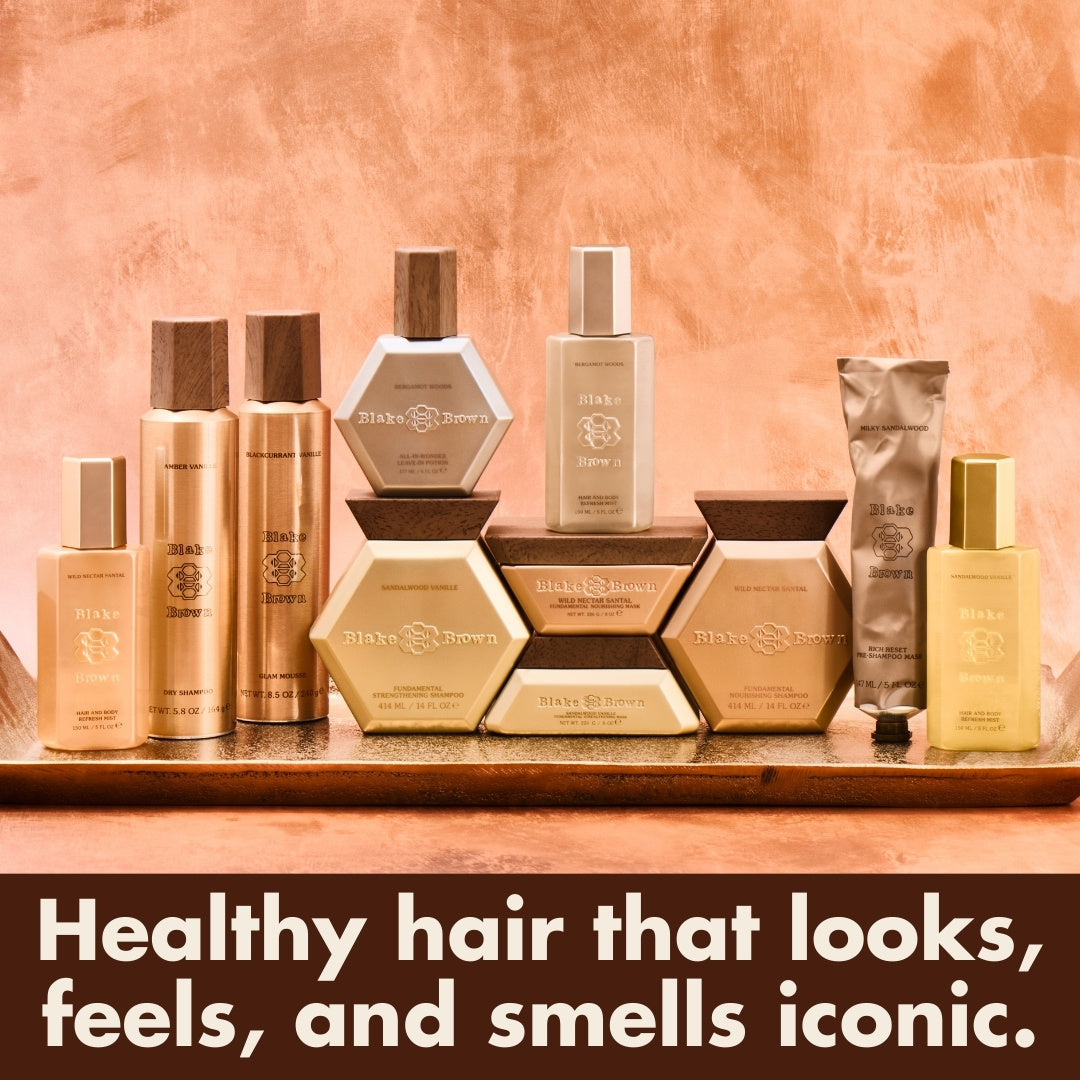 Full Blake Brown haircare collection displayed against a warm, peach-toned backdrop, featuring shampoos, masks, refresh mists, and styling products with the line 'Healthy hair that looks, feels, and smells iconic.'