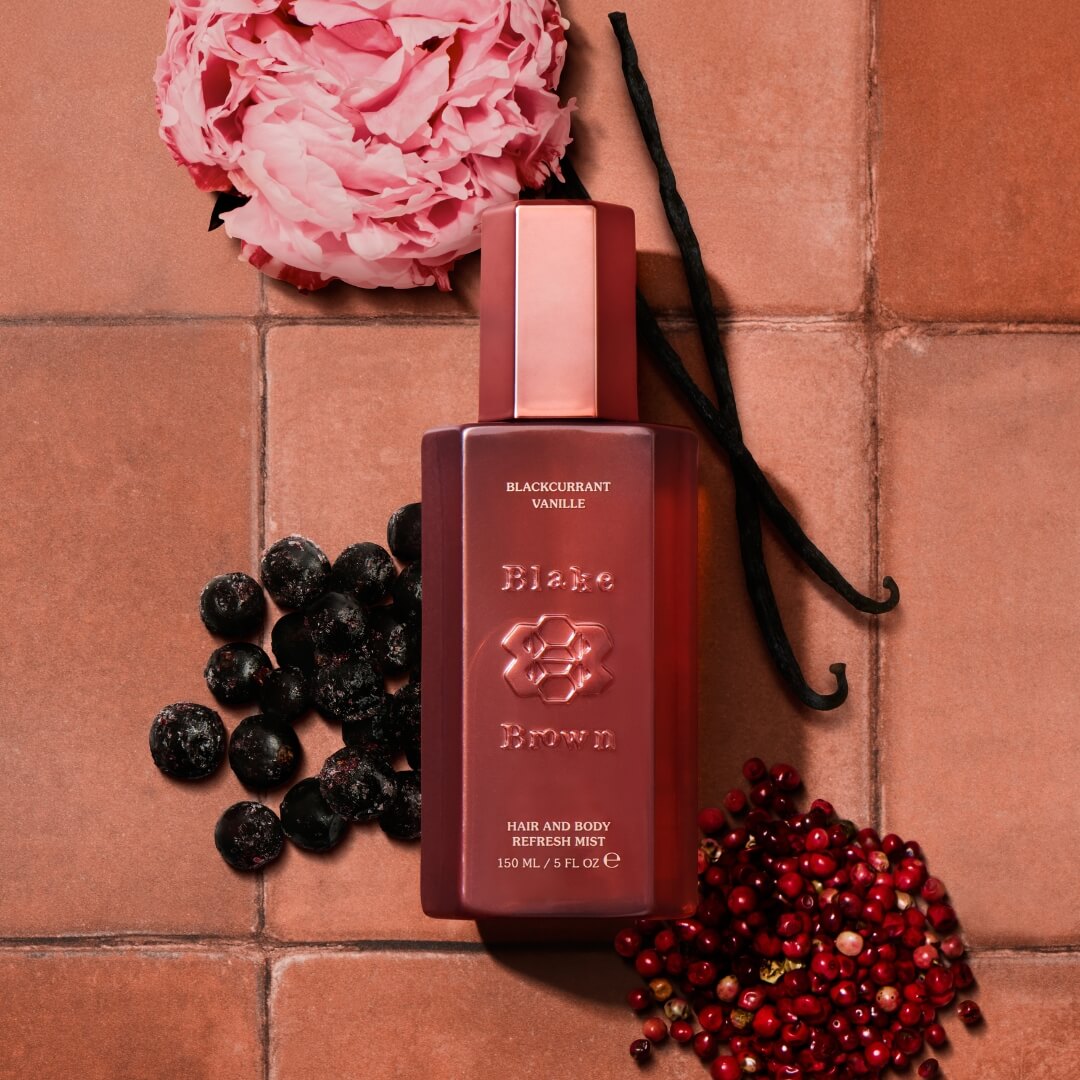 Red hair and body refresh mist bottle with vanilla beans, berries, and flowers on a tiled surface