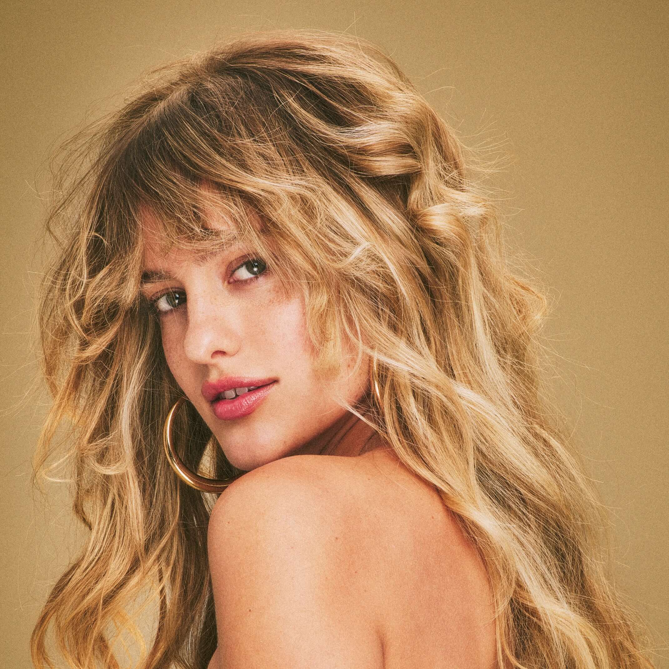 Blonde woman with luxurious wavy hair after using Blake Brown by Blake Lively haircare products, smiling in a headshot with a vintage filter.