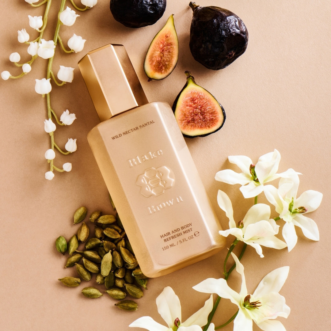 Blake Brown Hair and Body Refresh Mist in Wild Nectar Santal scent, surrounded by fresh figs, lily of the valley, cardamom pods, and white florals on a neutral background.
