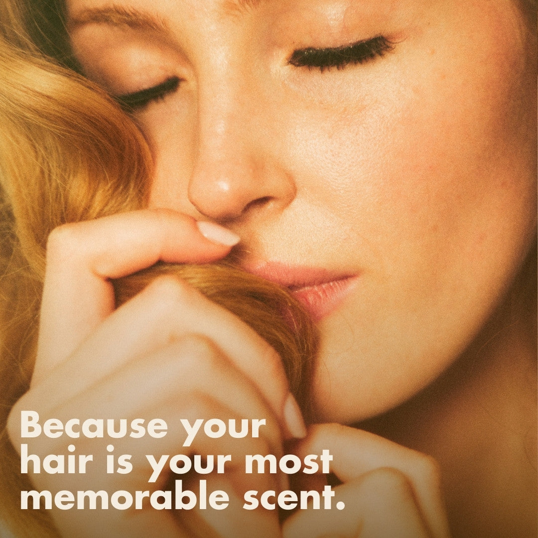 Close-up of a woman with closed eyes gently smelling her hair, accompanied by the text 'Because your hair is your most memorable scent'—highlighting Blake Brown's fragrances.