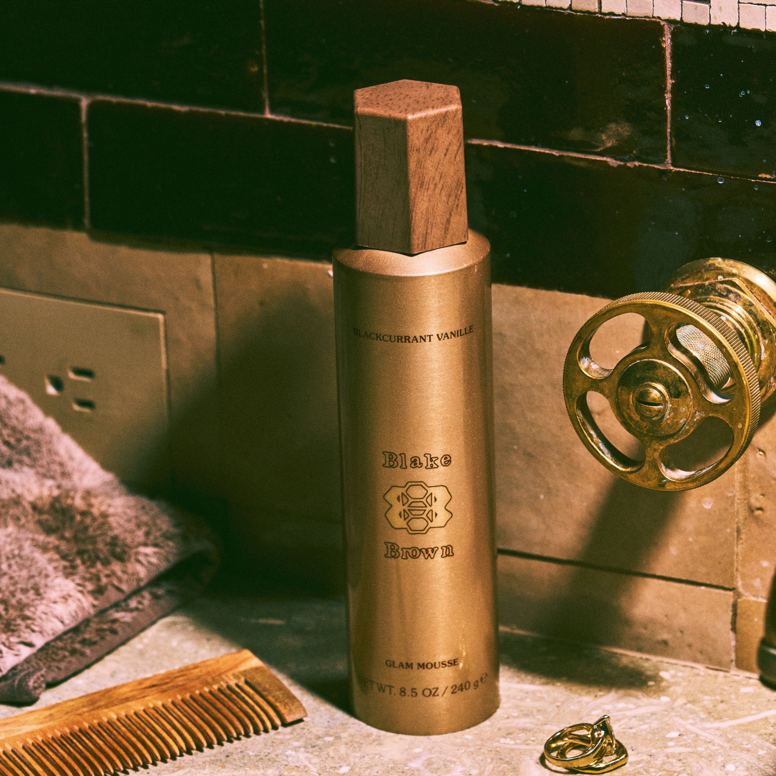 Blake Brown Glam Hair Mousse by Blake Lively, set in a shower scene of gold tones, showing off its elegant packaging.